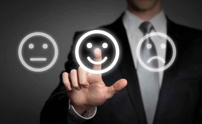 A man in a suit is pointing at a set of smiley faces.
