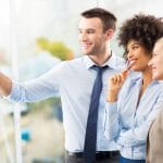 Three business people pointing at a whiteboard.