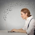 A woman is working on a laptop with musical notes coming out of it.