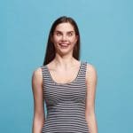 A woman in a striped tank top with a funny face with a blue background.
