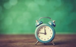 A blue alarm clock sits on a wooden table with a green background.