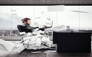 A man, overwhelmed by papers, sitting in a chair.