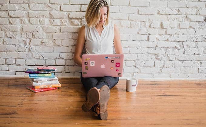 Woman using a pink laptop beside a pile of books and having a coffee.