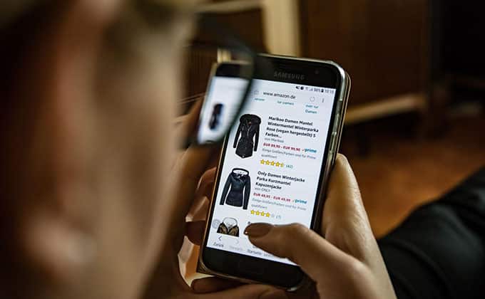 A woman is using a smart phone to look at clothes on a website, leveraging social media to drive sales for a small business.