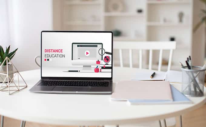 A laptop displaying a distance education screen sits on a white table with notebooks, a pen, and a potted plant in a bright room, highlighting how explainer videos can boost website engagement.