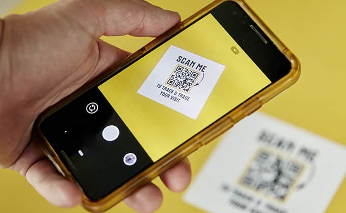 A hand holds a smartphone scanning QR codes on a paper labeled "SCAN ME"