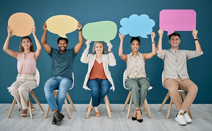 Five people sit in a row, each holding a colorful speech bubble sign above their head against a blue wall—perfect for creating engaging business Reels or TikTok content.