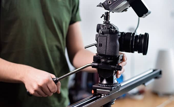 A person operating a professional camera mounted on a tripod slider, adjusting the equipment with their hand to capture dynamic shots perfect for business Reels.